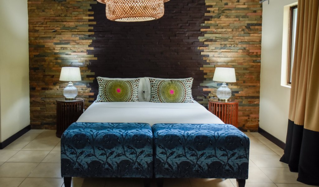 Bedroom with blue ottomans, stone wall, and a woven light fixture at Omali.