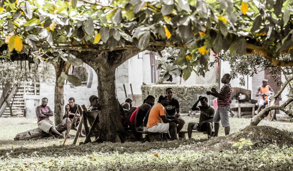Locals sitting together under a tree in front of Roca Sundy on Príncipe Island.