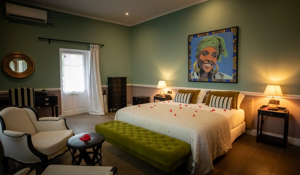 Belo Monte room with green walls, a framed portrait and an armchair seating area beside the bed