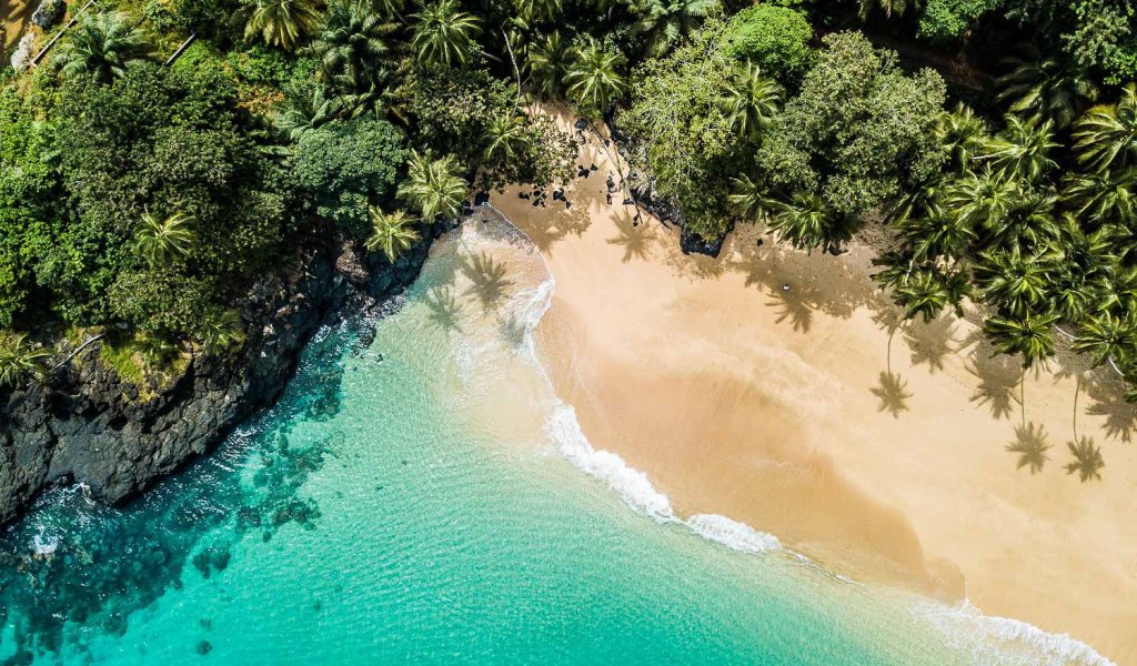 Aerial view of a secluded beach on Príncipe Island, with golden sand, turquoise waters and volcanic rocks framed by coconut palms