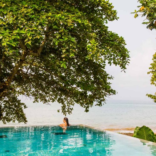 Mulher na piscina infinita turquesa, vista para o mar e uma árvore at Sundy Praia