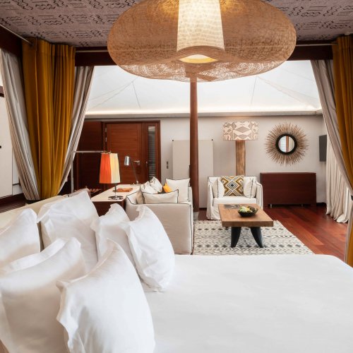 Quarto com cama de casal elegante, tapete artístico, área de estar e mesa ao fundo no Sundy Praia.