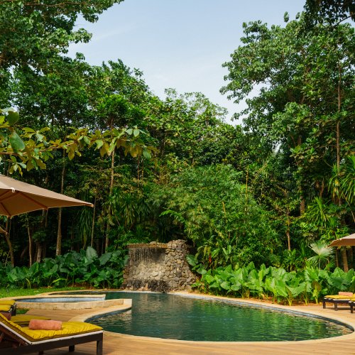 Piscina do Belo Monte com cascata de pedra, espreguiçadeiras e chapéus de sol rodeada pela floresta tropical