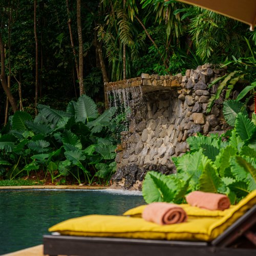 Espreguiçadeira junto à piscina do Belo Monte, ao lado de uma cascata de pedra e plantação tropical