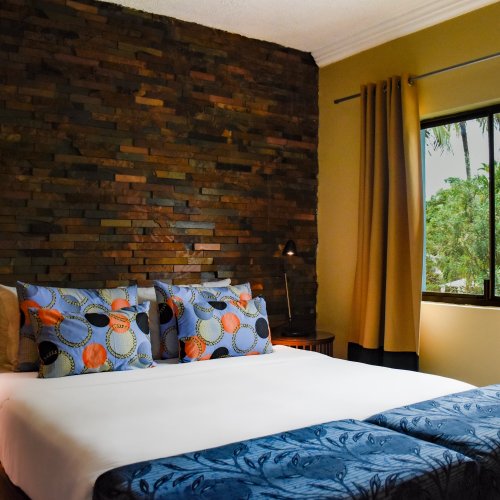 Bedroom with blue ottomans, stone wall, and a woven light fixture at Omali.