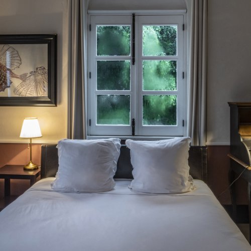 Cozy bedroom at Roça Sundy featuring a bed, a desk, a window with greenery view, and soft lighting