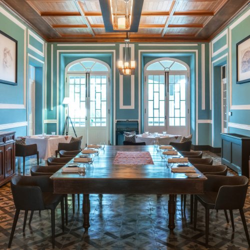 Elegant dining area at Roça Sundy with a long wooden table, art on the walls, and large windows
