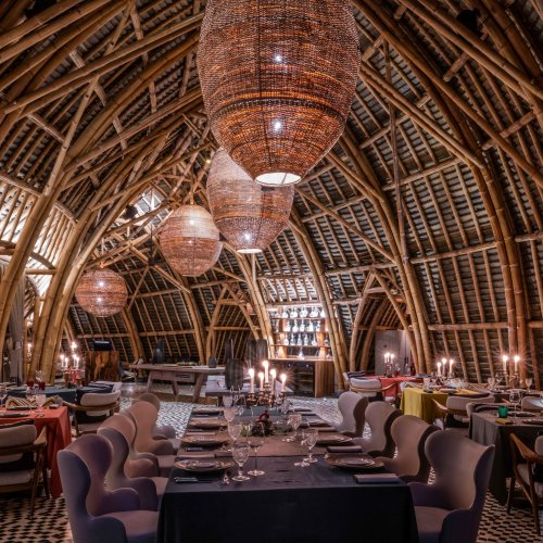 Vista interior do restaurante OKA Sundy com arquitetura de bambu, iluminação decorativa e mesas de jantar