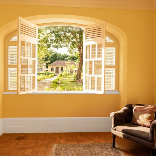 Sunlit window at Belo Monte opening to the courtyard gardens with yellow buildings and a cosy armchair inside.
