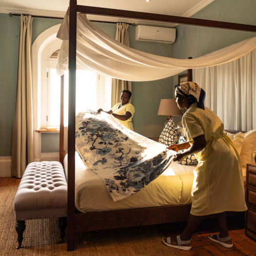 Housekeeping preparing a four-poster bed with floral cover in the Panoramic Suite at Belo Monte, soft morning light.