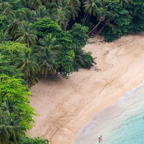 Aerial view of Praia Banana near Hotel Belo Monte, two guests in turquoise shallows for a calm swim