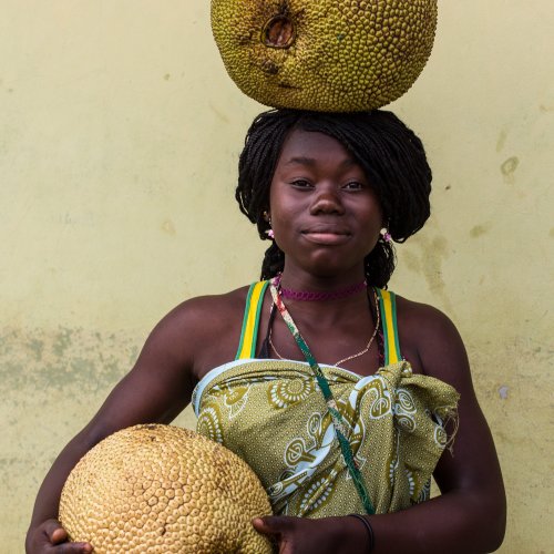 Portrait of a smiling woman balancing a large fruit on her head