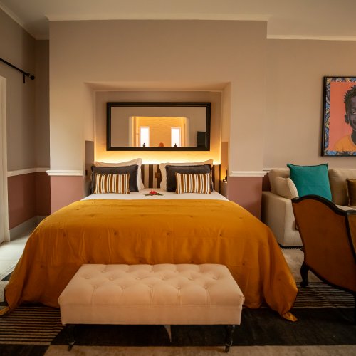 Belo Monte bedroom with an ochre bedspread, framed portrait and garden view through tall windows
