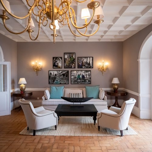 Belo Monte lounge with a gold chandelier, framed island photography and a sea view through arched French doors