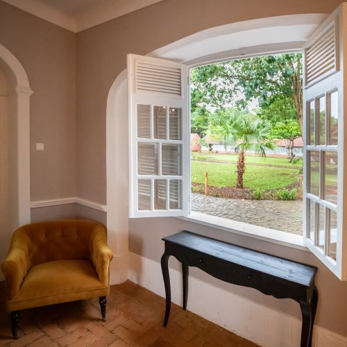 Belo Monte room with an ochre velvet armchair and an open shuttered window overlooking the garden