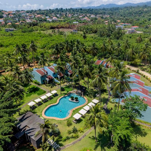 Vista aérea da zona da piscina e quartos do Omali rodeados de palmeiras, com a cidade de São Tomé ao fundo