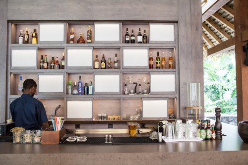 Um bar de bebidas com garrafas em prateleiras e um homem a trabalhar atrás do balcão at Sundy Praia
