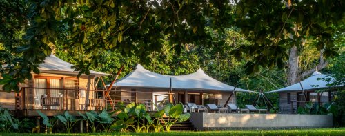 View of the 3-bedroom pool villa at Sundy Praia with tented roofs, garden furniture, and rainforest in the background.