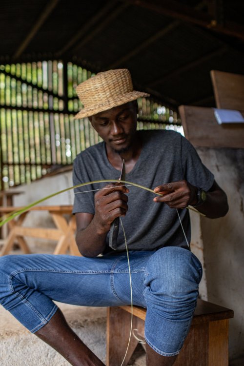 Local man in a hat and jeans weaving baskets on Príncipe Island.