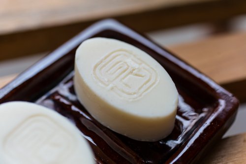 Two handmade white soaps by Paciencia Cosmetics with the logo on top.