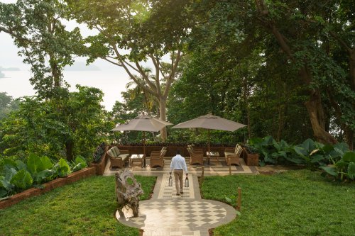 Staff member crossing a garden terrace with parasols and sea view at sunset, Belo Monte