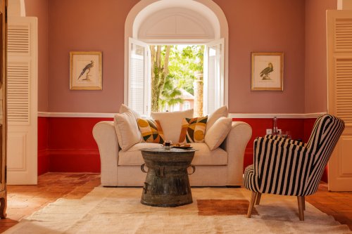 Belo Monte sitting room with a linen sofa, striped armchair and framed parrot prints by an open window
