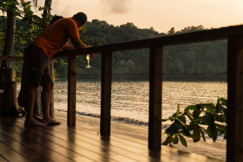 A man holding a drink at the beach during sunset at Bom Bom Beach Resort.