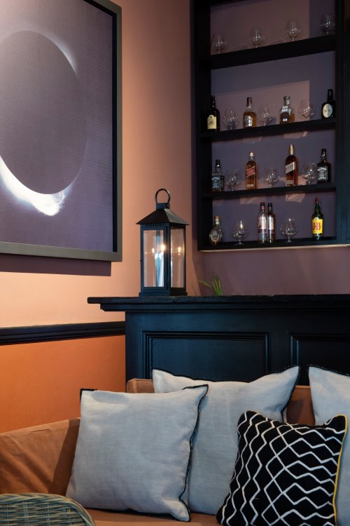 Bar acolhedor na Roça Sundy com um sofá, almofadas e uma exposição de garrafas e copos