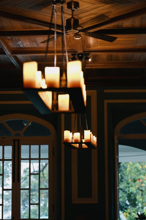 Hanging candlelight fixture with a wooden ceiling and window in the background at Roça Sundy