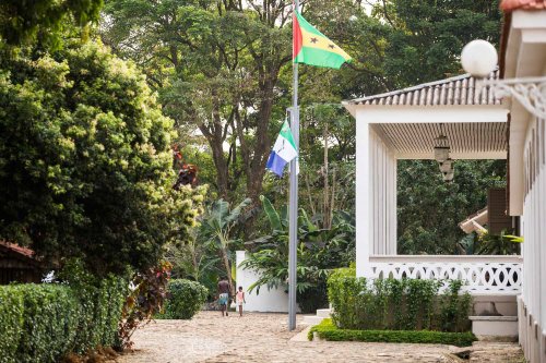 Vista exterior da entrada da Roça Sundy com pilares brancos, janelas arqueadas e vegetação exuberante