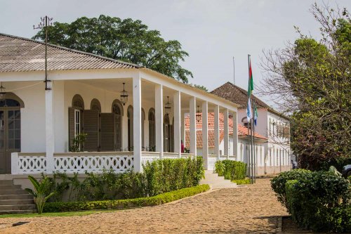 Exterior view of Roça Sundy entrance with white pillars, arched windows, and lush greenery