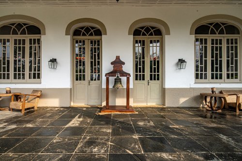 Entrada da Roça Sundy com portas de estilo colonial, um sino e cadeiras de madeira na varanda