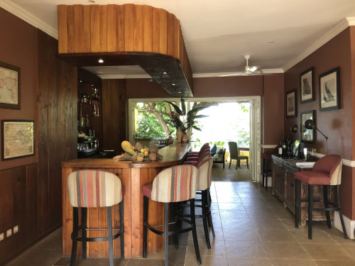 Heritage bar at Belo Monte with wooden counter, striped stools and an open terrace framed by tropical greenery.