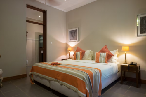 Spacious Garden Room with king bed, striped bedspread and soft lamps, doorway leading to the ensuite bathroom.