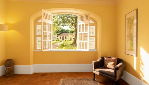 Janela iluminada no Belo Monte com vista para os jardins do pátio e edifícios amarelos, poltrona acolhedora no interior.