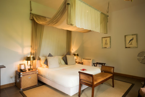 Panoramic Suite bedroom with canopy bed, warm lamps and leather bench, framed bird prints on the wall.
