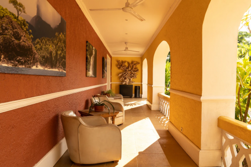 Sunny arcade porch at Belo Monte with arches, armchairs and wall art, looking onto tropical plants.