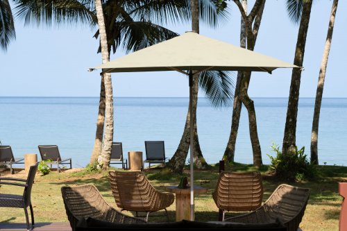 Cadeiras de vime e chapéu de sol na esplanada do Bom Bom Beach Club, com palmeiras e o oceano ao fundo, Ilha do Príncipe