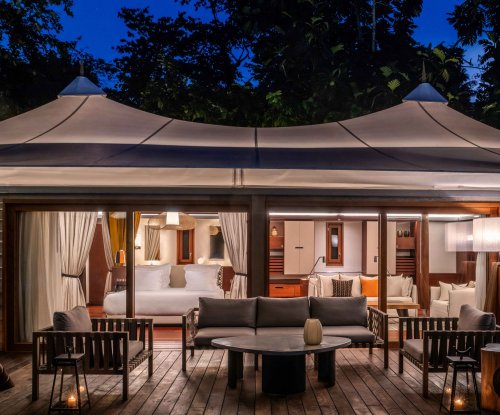 Exterior view of the tent villa at Sundy Praia by night, with the illuminated bedroom in the background and the terrace in the foreground.