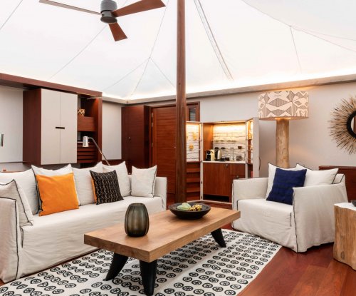 Quarto com cama de dossel elegante, tapete artístico, área de estar e mesa de madeira em primeiro plano na tenda-vila Sundy Praia.