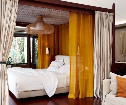 Vista da elegante cama de casal numa tenda-vila no Sundy Praia, com mesa de madeira, vasos e um tapete amarelo-preto em primeiro plano.