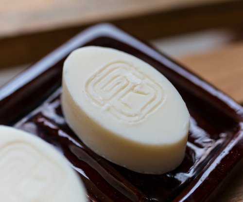 Two handmade white soaps by Paciencia Cosmetics with the logo on top.
