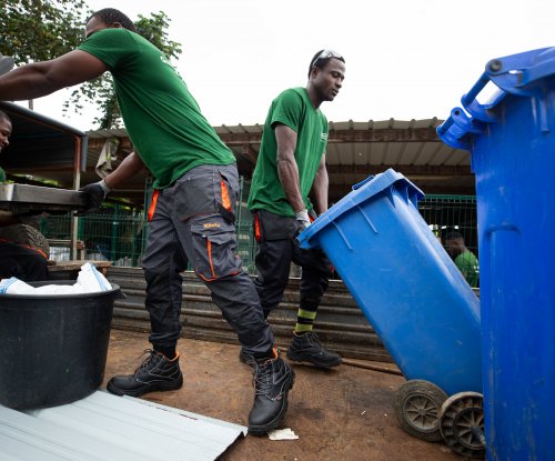 Três trabalhadores com camisetas verdes a reciclar com contentores azuis na Ilha do Príncipe.