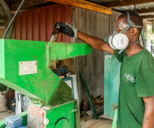 Worker in dark green HBD T-shirt, respirator, and goggles recycles glass with a machine on Príncipe Island.