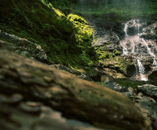 Waterfall flows over rocks on Príncipe Island, partly covered in green moss.