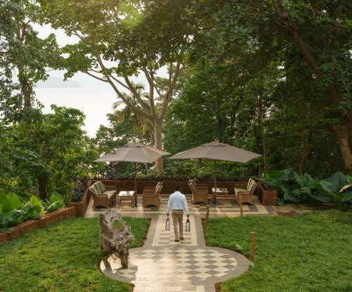 Staff member crossing a garden terrace with parasols and sea view at sunset, Belo Monte