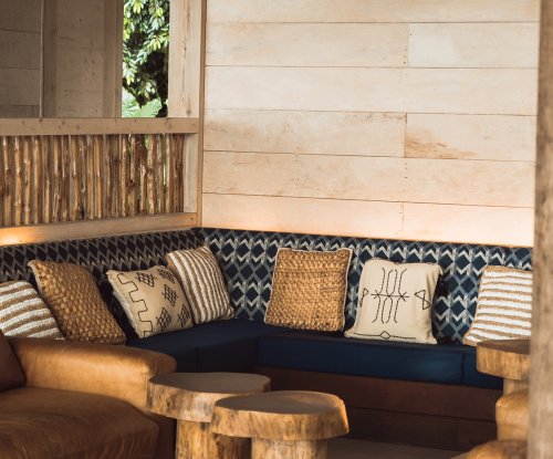 Cantinho de lounge com sofás de couro, almofadas tecidas e mesas de madeira no Bom Bom Beach Club