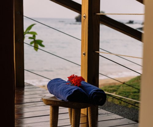 Beach towels on a small wooden bench with a view of the ocean from a bungalow at Bom Bom Resort