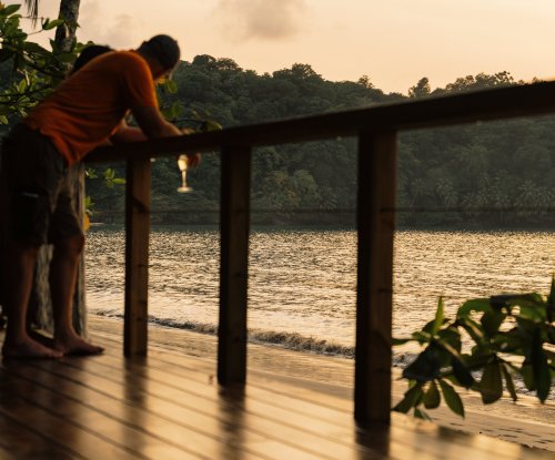 A man holding a drink at the beach during sunset at Bom Bom Beach Resort.