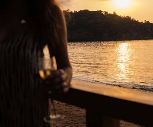 A man holding a drink at the beach during sunset at Bom Bom Beach Resort.